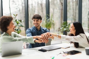 Tres profesionales uniendo las manos sobre una mesa de trabajo